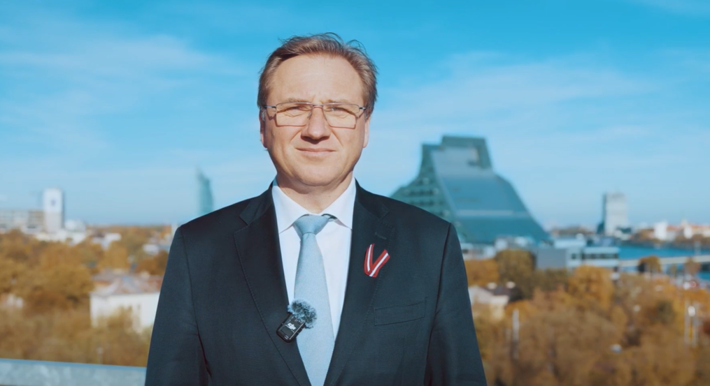 Rektors Gundars Bērziņš ar Latvijas karoga lentīti pie drēbēm. Fonā Latvijas Nacionālā bibliotēka.